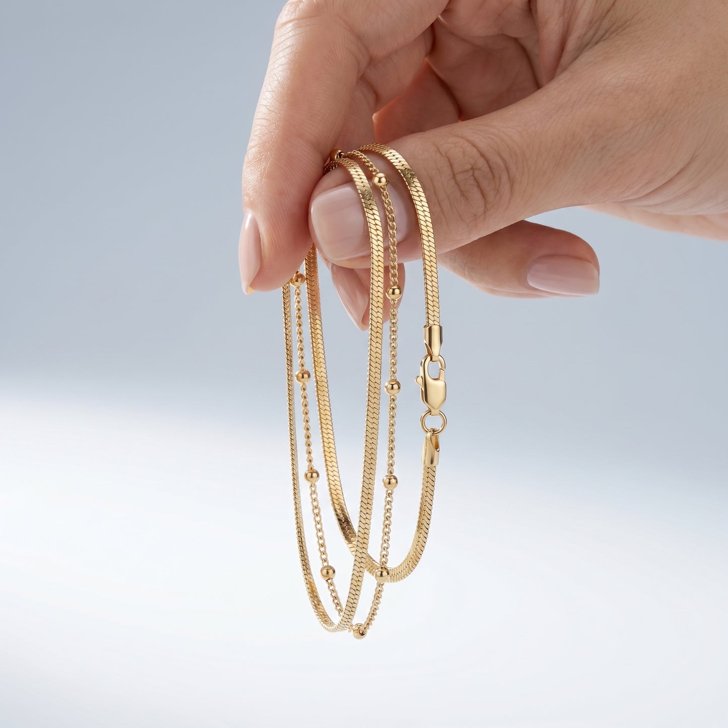 Cavigliera Layered Doppia Oro 18K - scala reale tra le dita di una mano - UpperEast Jewels