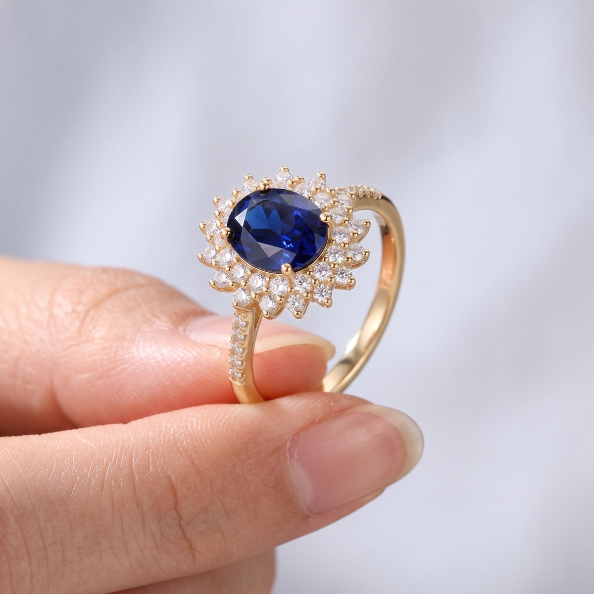 Anillo con piedra azul y circonitas bañado en oro de 18K sostenido entre los dedos, para ver el tamaño real