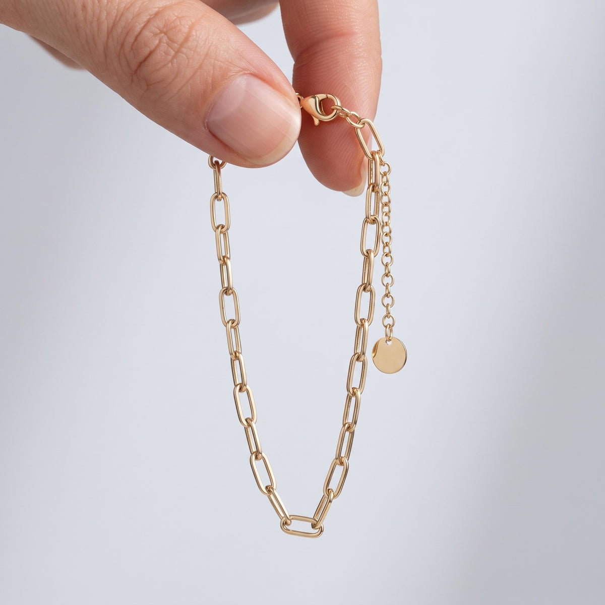 Bracciale a catena paperclip placcato oro 18K tenuto tra le dita, per vedere le dimensioni reali