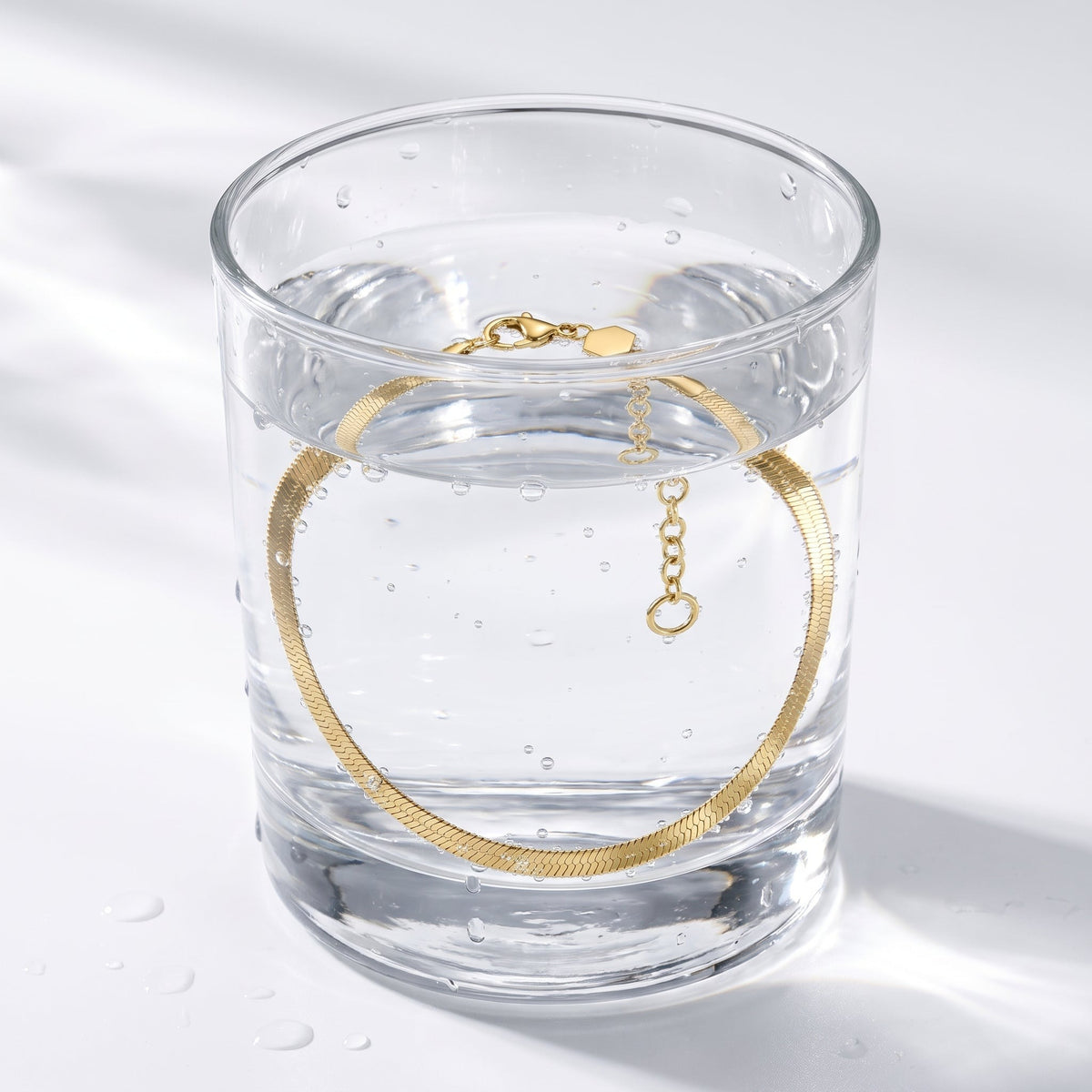 Pulsera de cadena snake plana bañada en oro de 18K en un vaso de agua