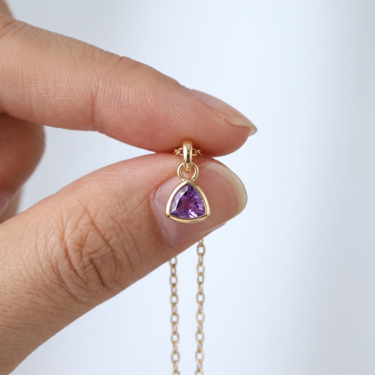 Collar con piedra del mes bañado en oro de 18K sostenido entre los dedos, para ver el tamaño real